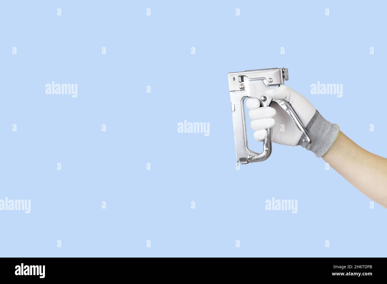 Gloved hands holding stapler construction tools. Work tools on blue background Stock Photo