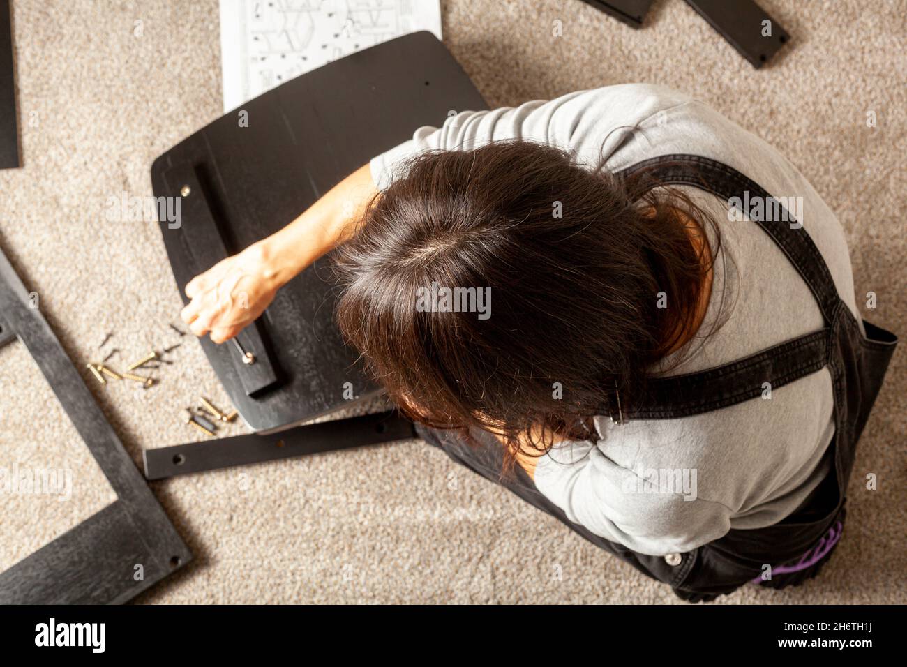 DIY furniture assembly concept including a caucasian person sitting on carpet floor with pieces of furniture, trying to assemble it based on instructi Stock Photo