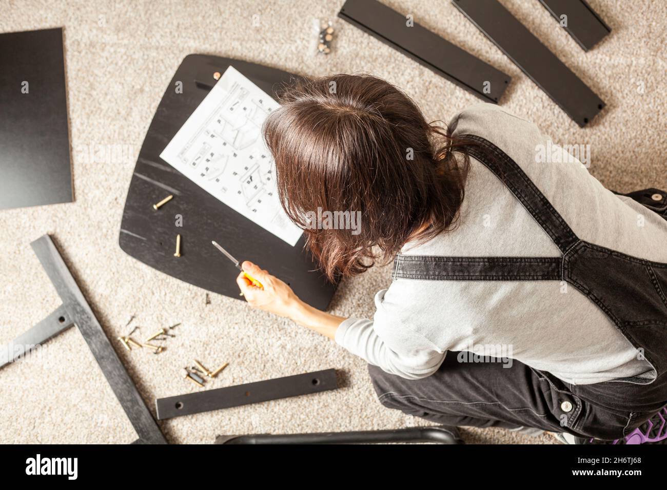 DIY furniture assembly concept including a caucasian person sitting on carpet floor with pieces of furniture, trying to assemble it based on instructi Stock Photo