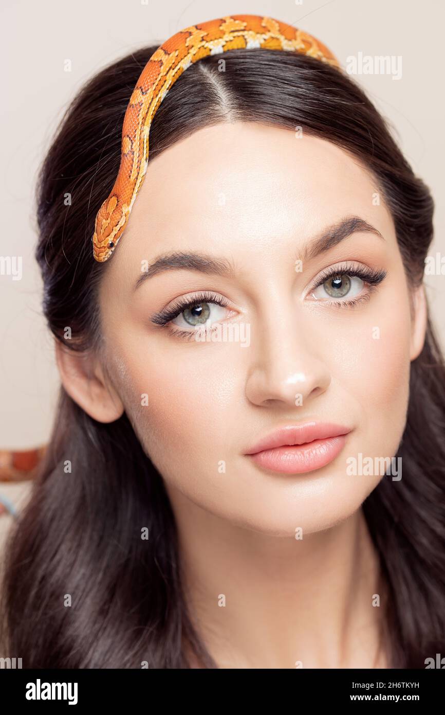 Fashion portrait of young brunette woman with snake on her head, symbol of youth, beauty, skin elasticity and anti-wrinkle cream. Stock Photo