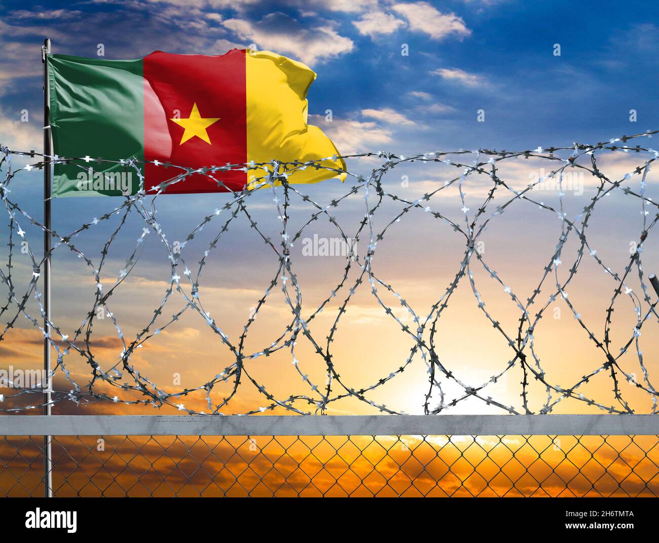 A fence with barbed wire against the background of a colorful sky and a flagpole with the flag of Cameroon protects the state's border from illegal mi Stock Photo