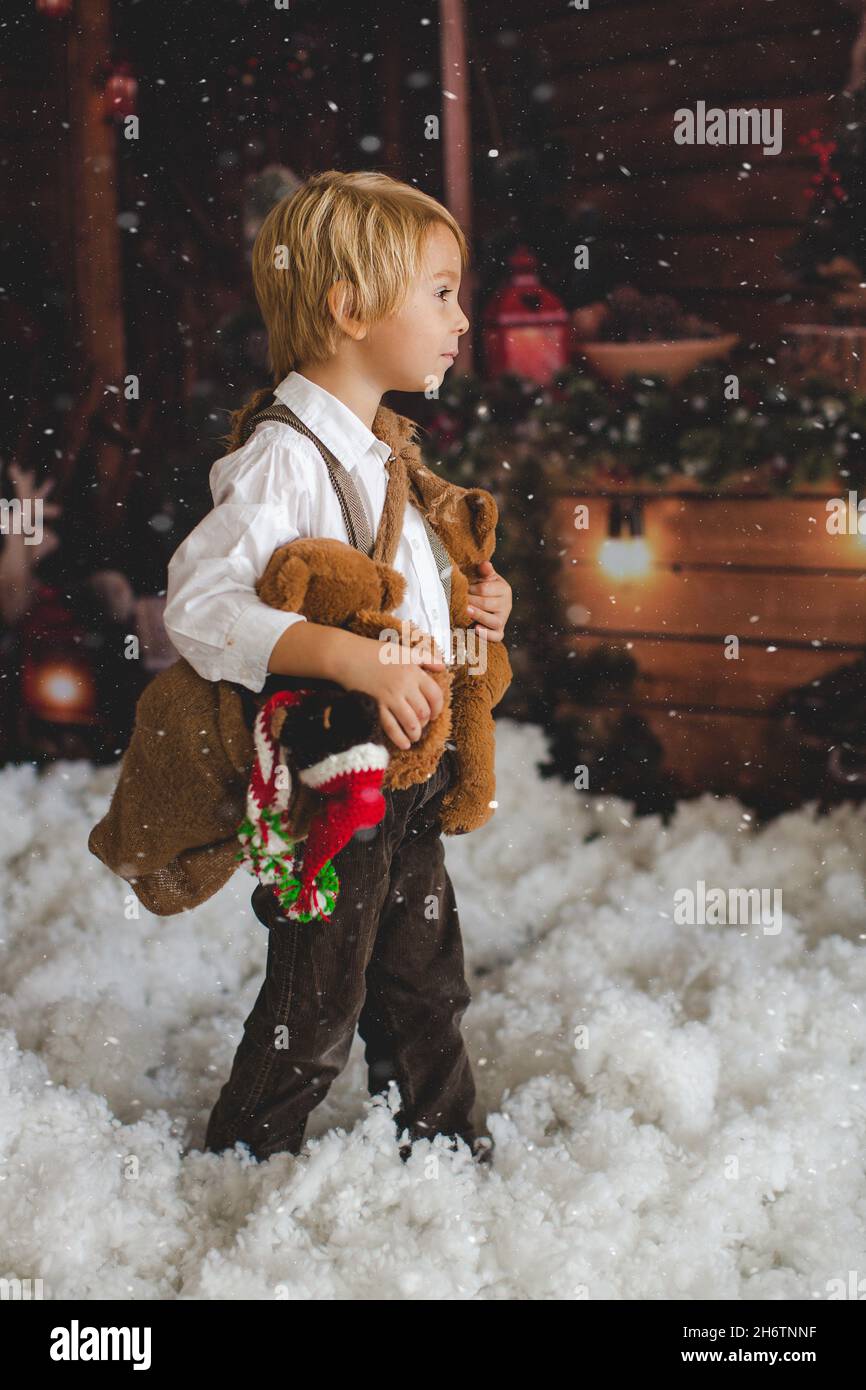 Cute fashion toddler boy, playing in the snow with teddy bear in front ...