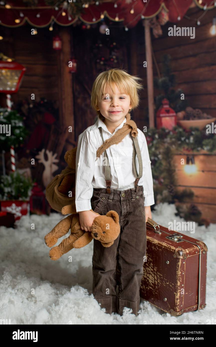 Cute fashion toddler boy, playing in the snow with teddy bear in front ...