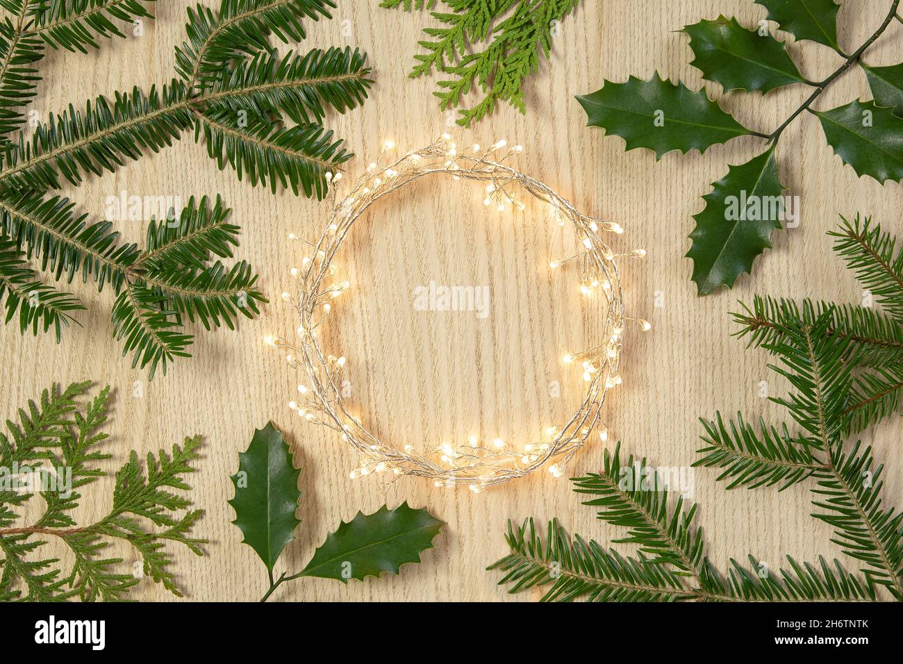 Flat lay top view, Christmas background circle shape border frame, light garland and fir twigs wooden background. Stock Photo