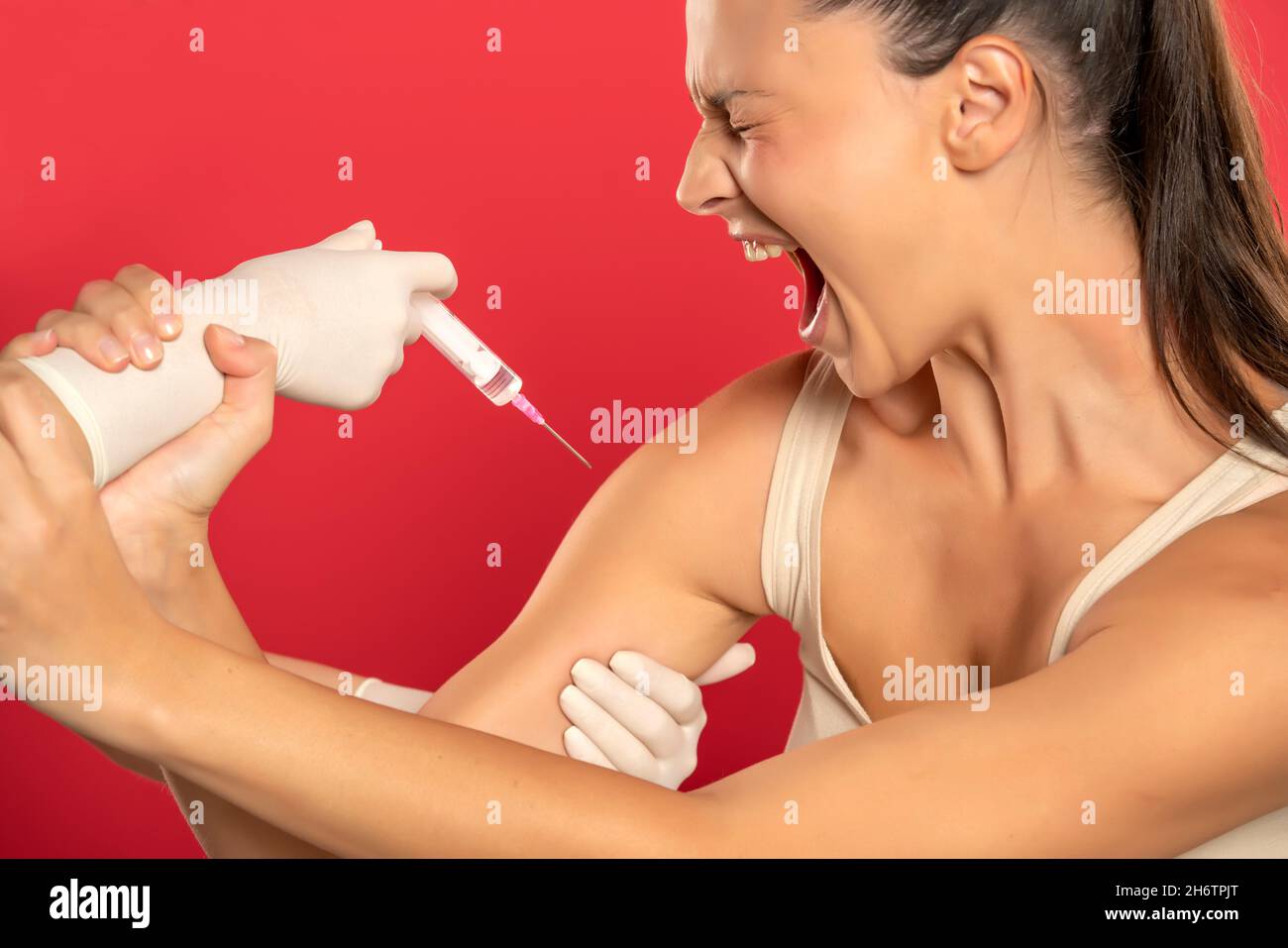 a young screaming woman refuses to be vaccinated on a red background Stock Photo