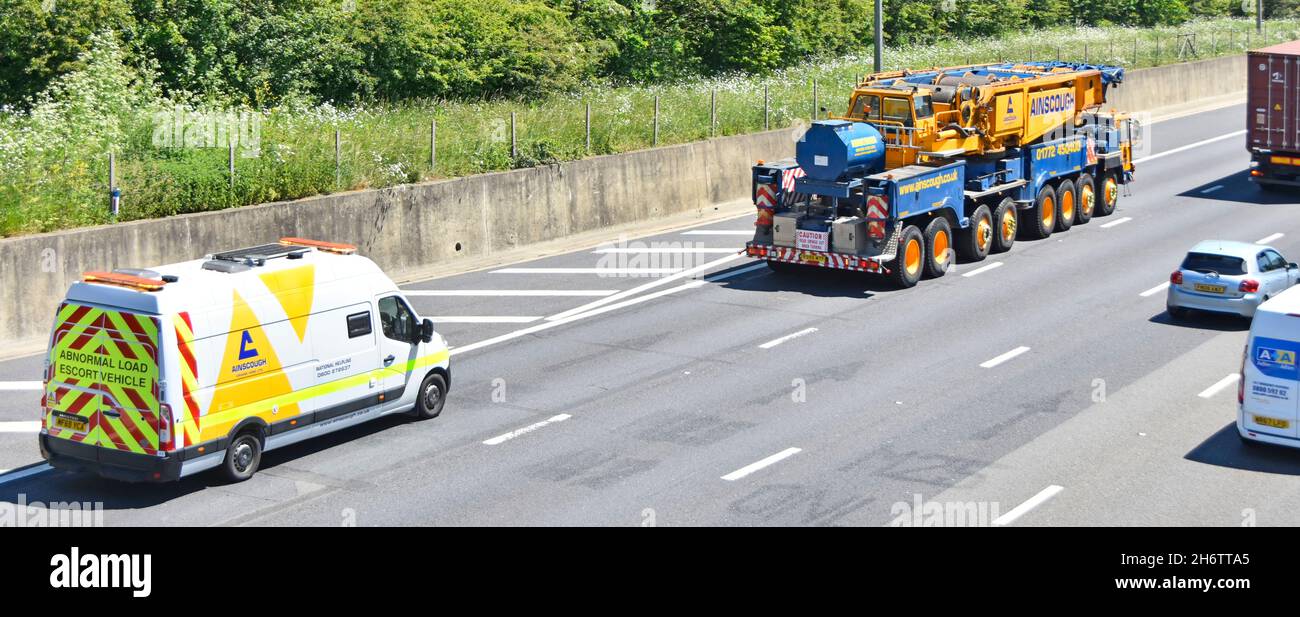 Aerial view large slow heavy lift Ainscough mobile crane driving up gradient with Renault Master van abnormal load escort warning vehicle UK motorway Stock Photo