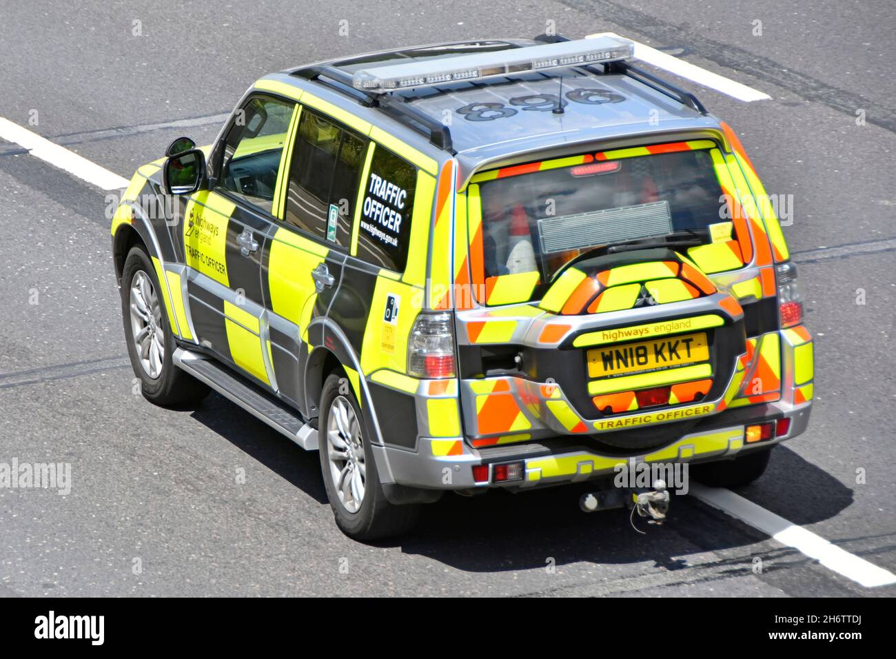 Aerial side and back view traffic officer driver inside high visibility patrol car signals to change lane driving along M25 motorway Essex England UK Stock Photo