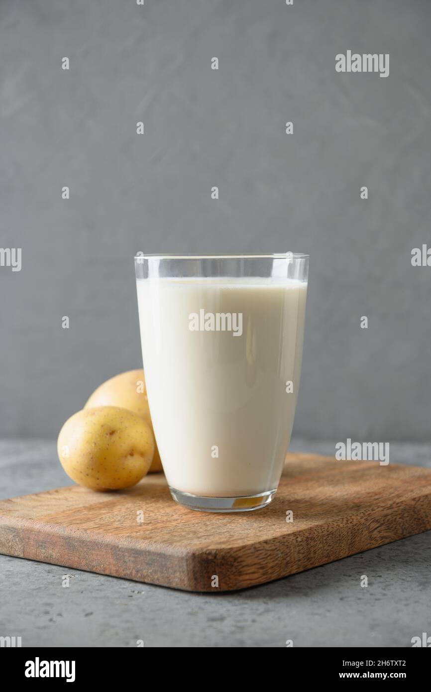 Vegan potato milk in glass and potato in bowl on gray background. Vertical format. Close up. Plant based milk replacer and lactose free. Stock Photo