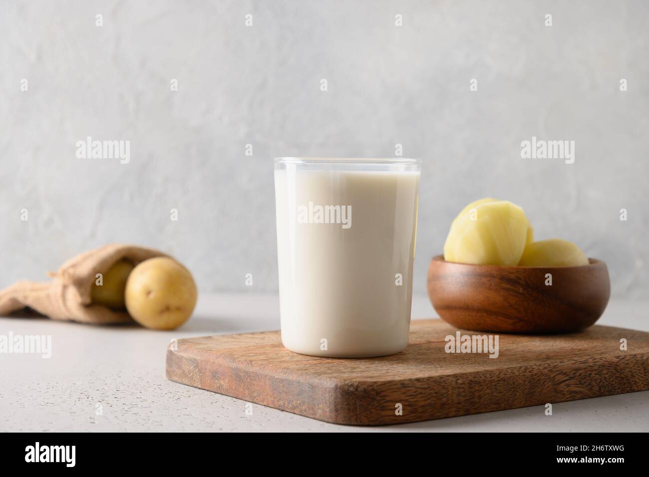Vegan potato milk in glass and potato in bowl on light background. Close up. Plant based milk replacer and lactose free. Stock Photo