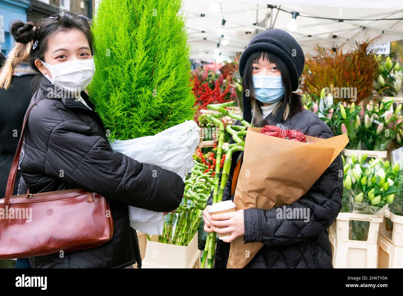 Columbia Road Flower Market young Asian women plants facemasks in street at market stalls on Sunday in November 2021 East London UK KATHY DEWITT Stock Photo