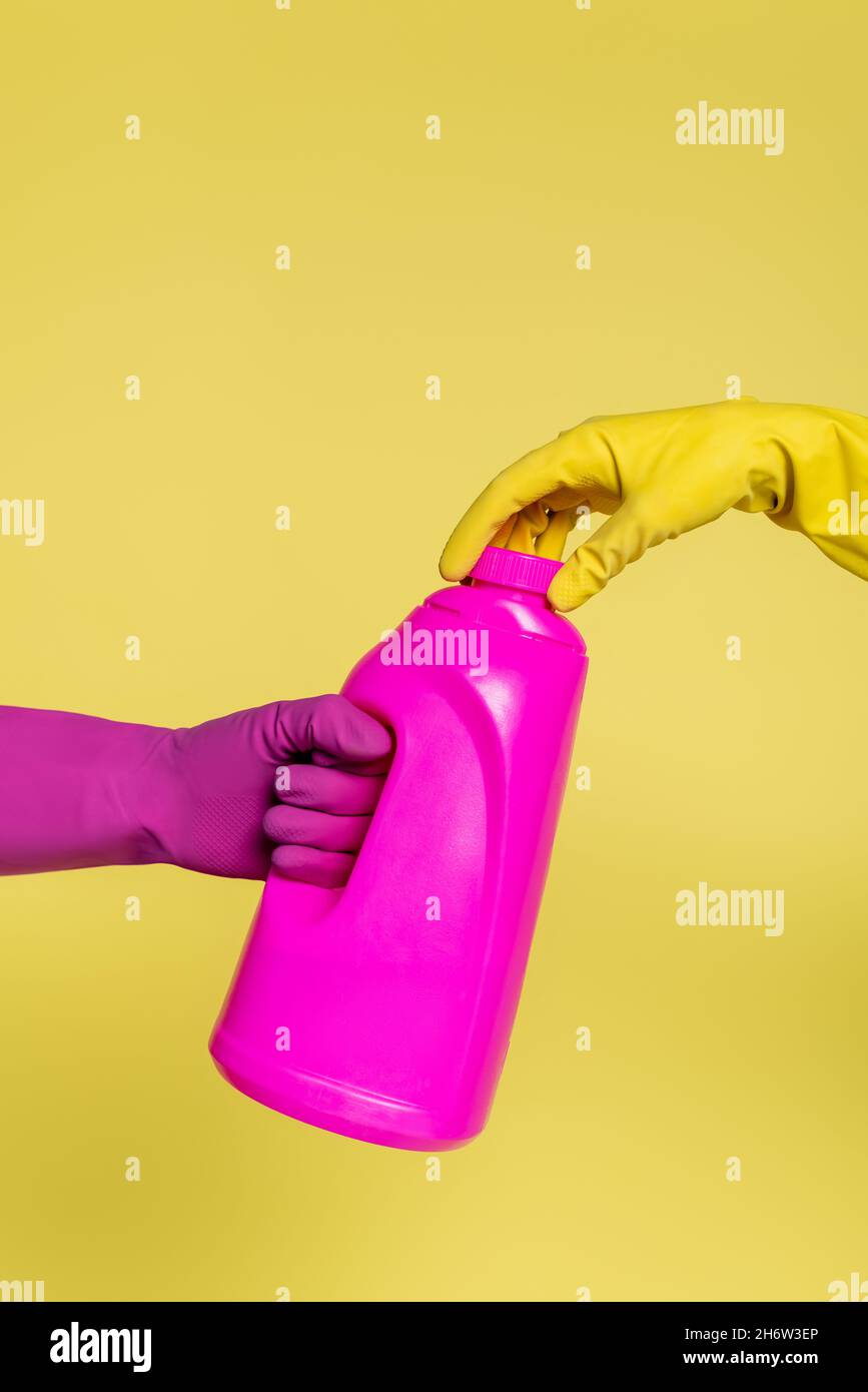 cropped view of people in rubber gloves holding pink bottle with detergent isolated on yellow Stock Photo