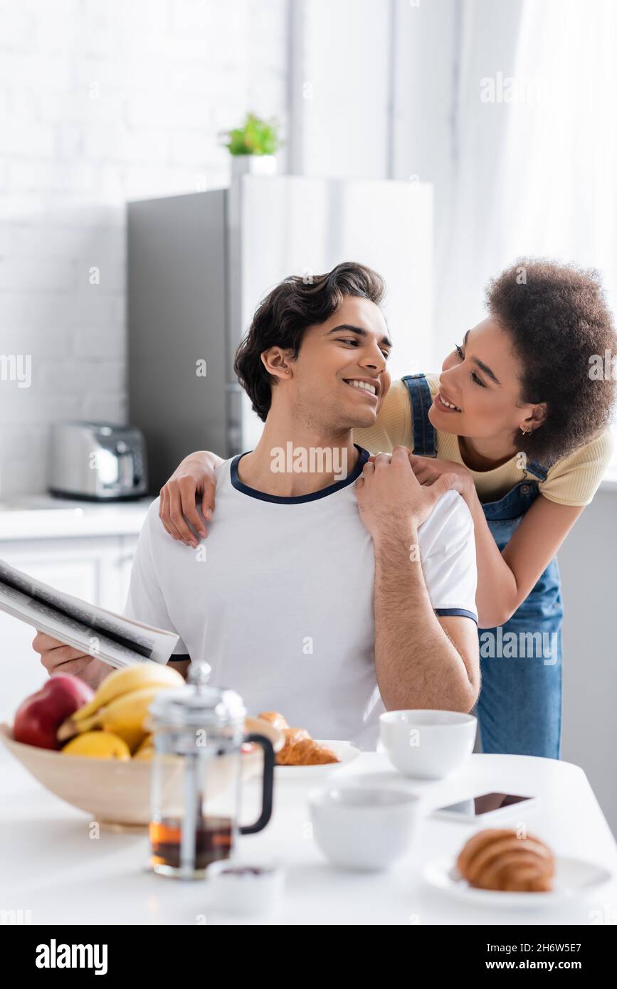 happy african american woman hugging boyfriend with newspaper at home ...