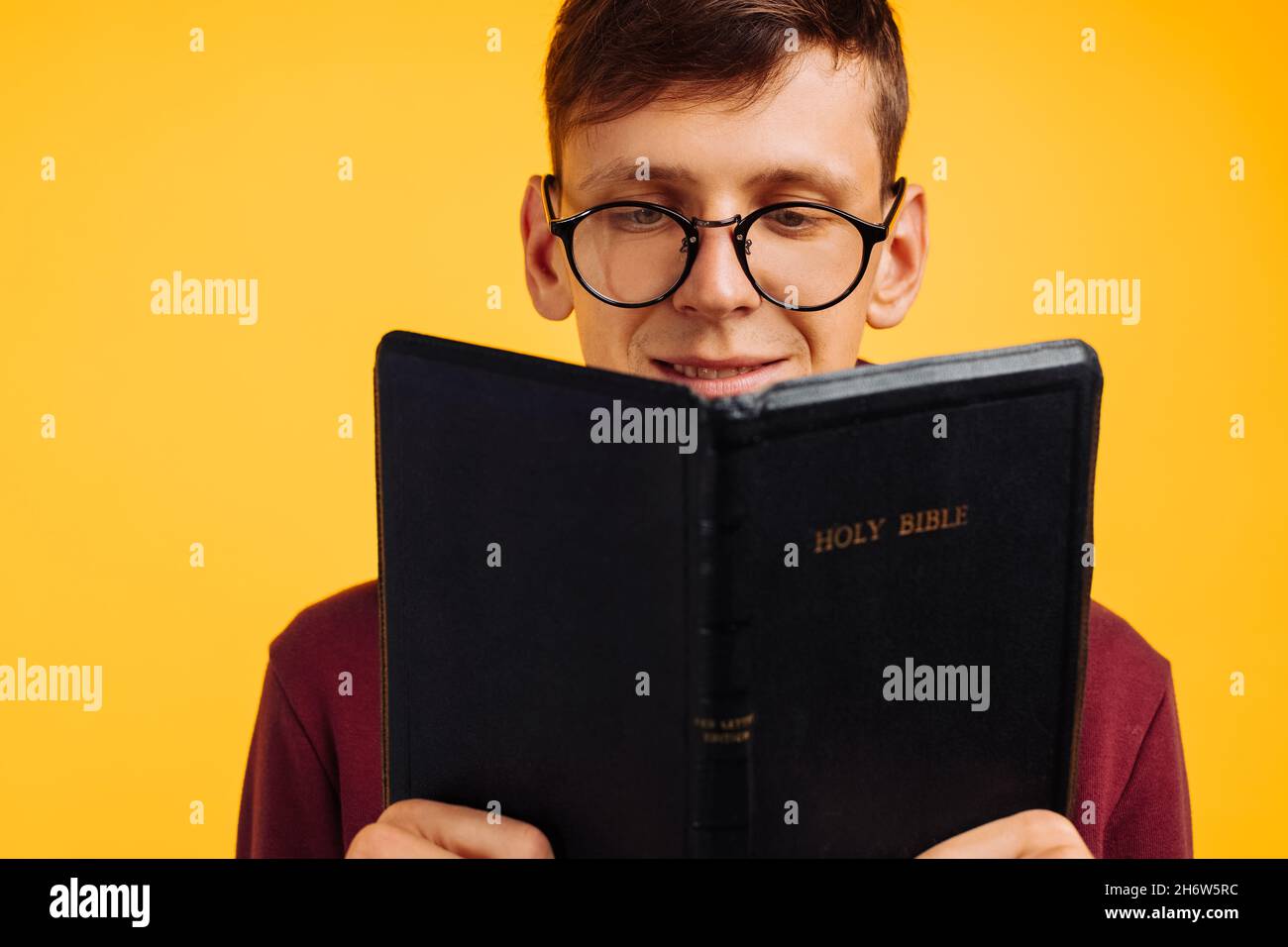 Christian man is reading and studying the Bible, the man is holding the Bible in his hands. Bible reading over isolated yellow background. Faith, spir Stock Photo