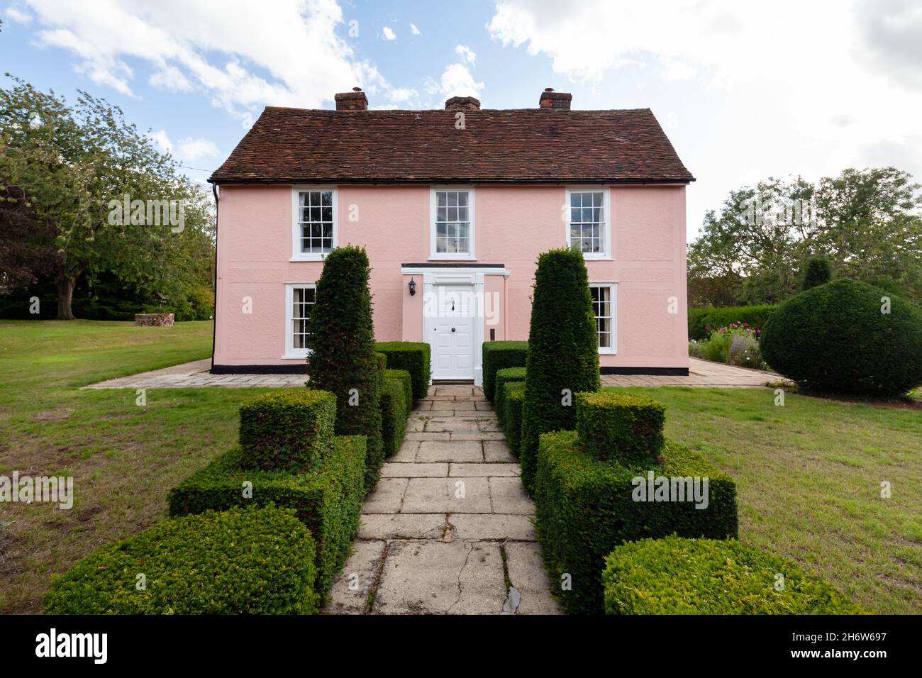 Wixoe, England - September 26 2019: Pink coloured country detached farmhouse with clipped shrubs and pathway leading to the from door and lawns to eit Stock Photo