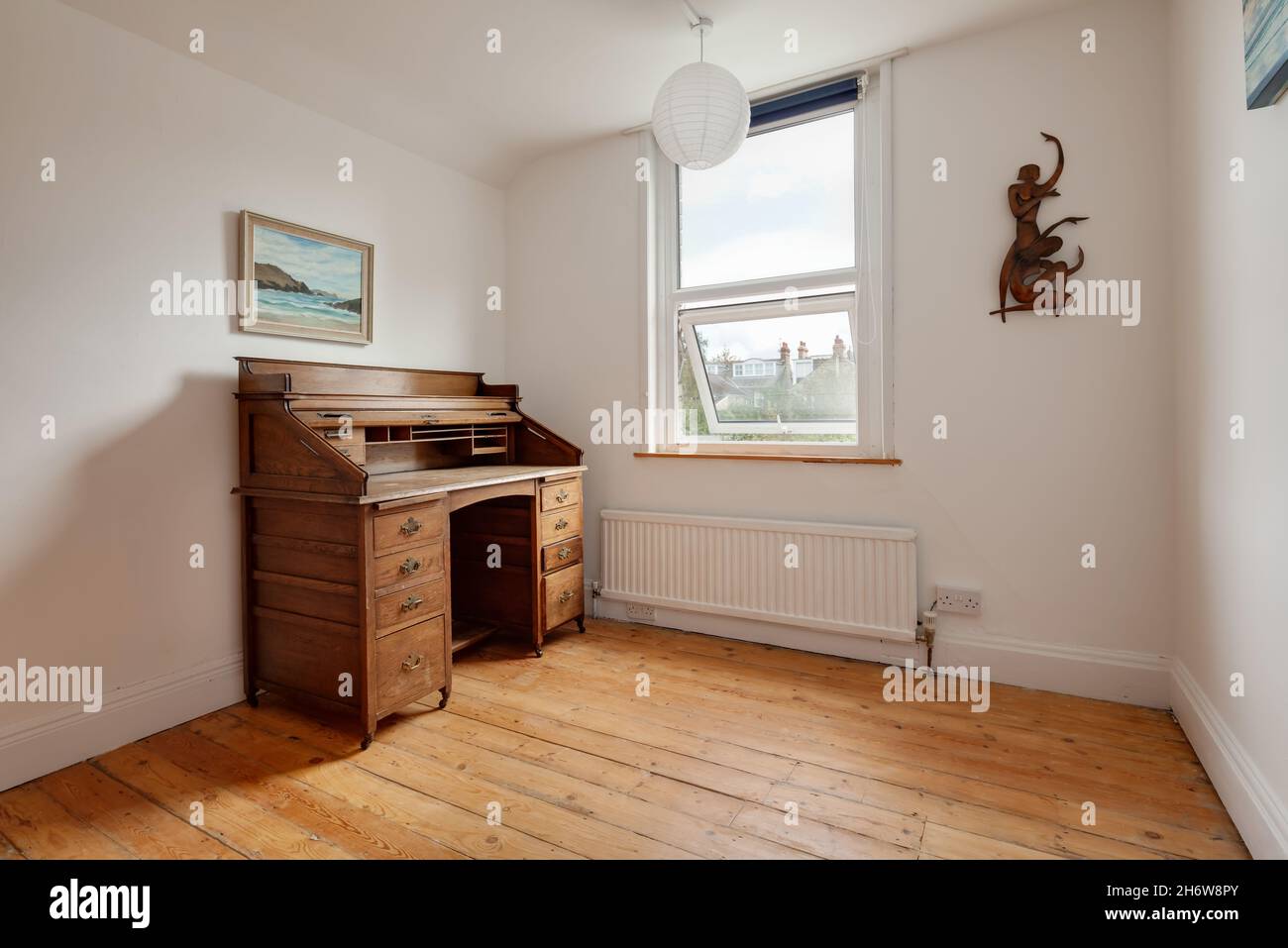 Cambridge, England - August 21 2019: Sparsely furnished room in Victorian era British home with traditional wooden bureau next to window. Stock Photo