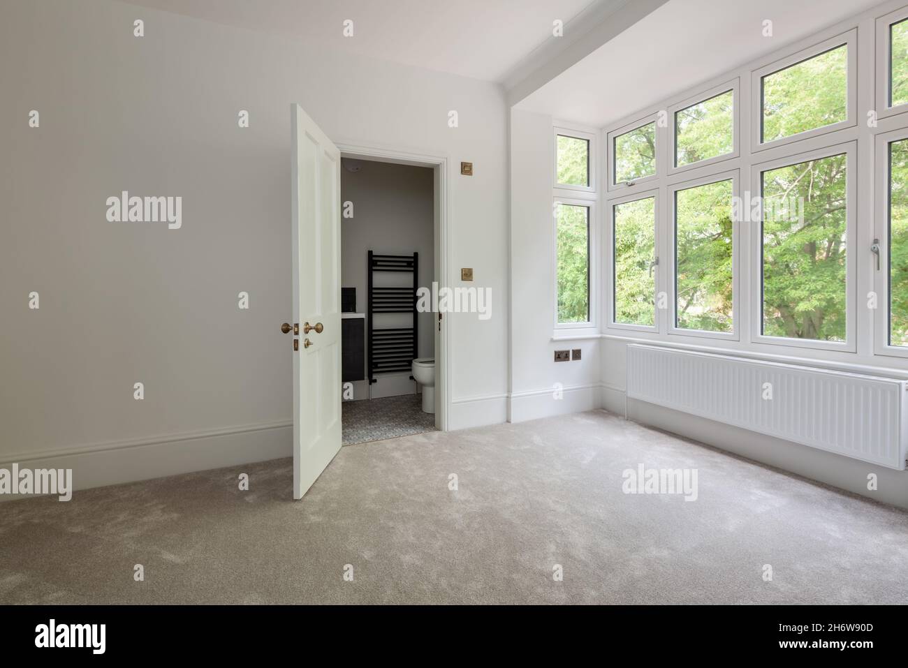 Wratting, England - August 19 2019: Empty bedroom space with door opening onto ensuite closet bathroom simply decorated in white with carpeted floor Stock Photo