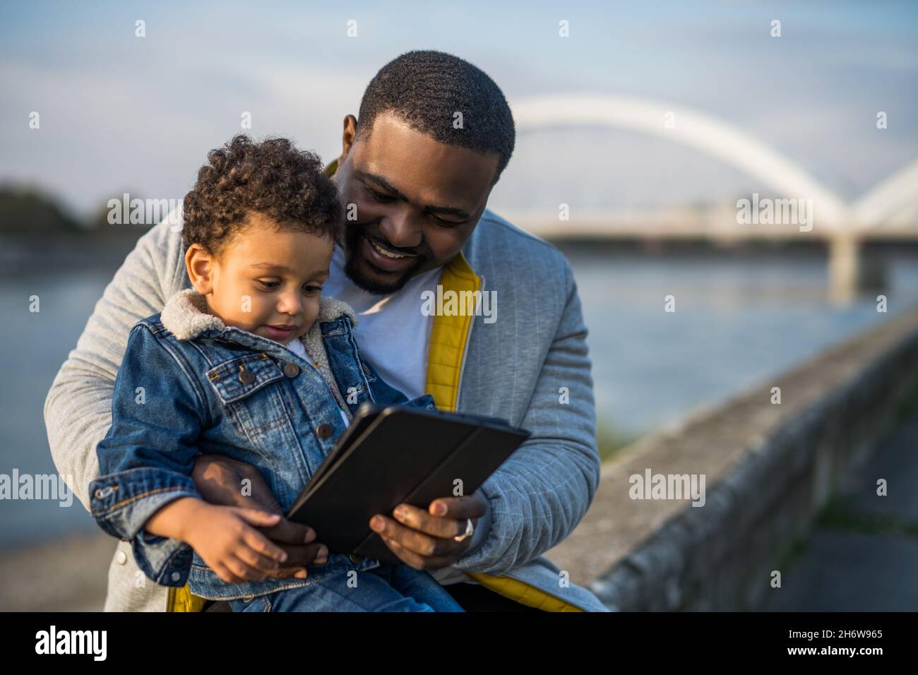 Father and his son using digital tablet while sitting together outdoor. Stock Photo