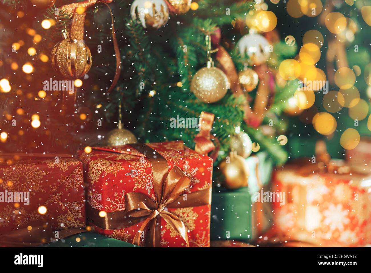 Many gift boxes standing under decorated Christmas tree with superimposed falling snow Stock Photo
