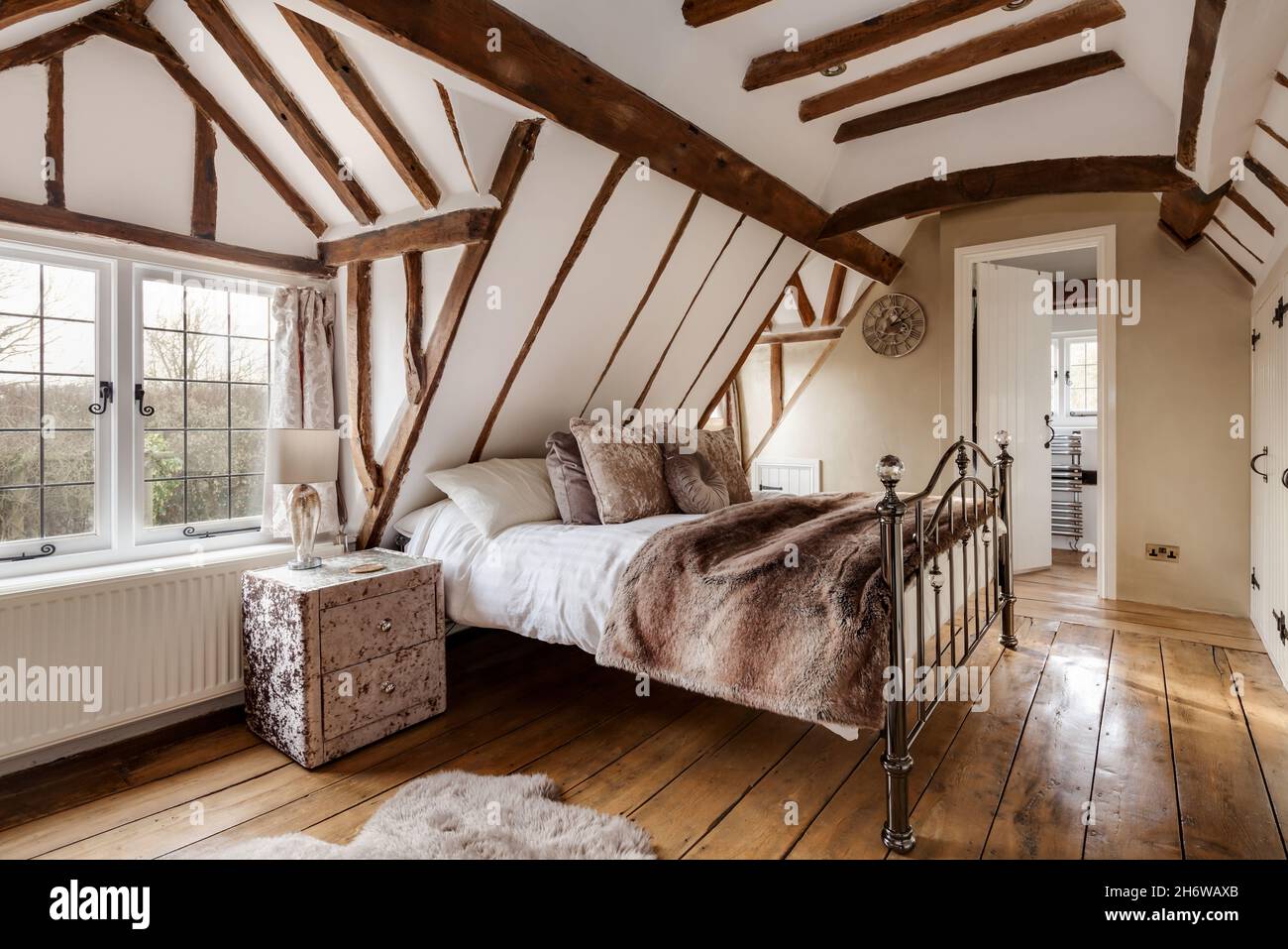 Essex, England - January 18 2019: Heavily beamed bedroom space with sloping ceilings and original floorboards with iron bed Stock Photo