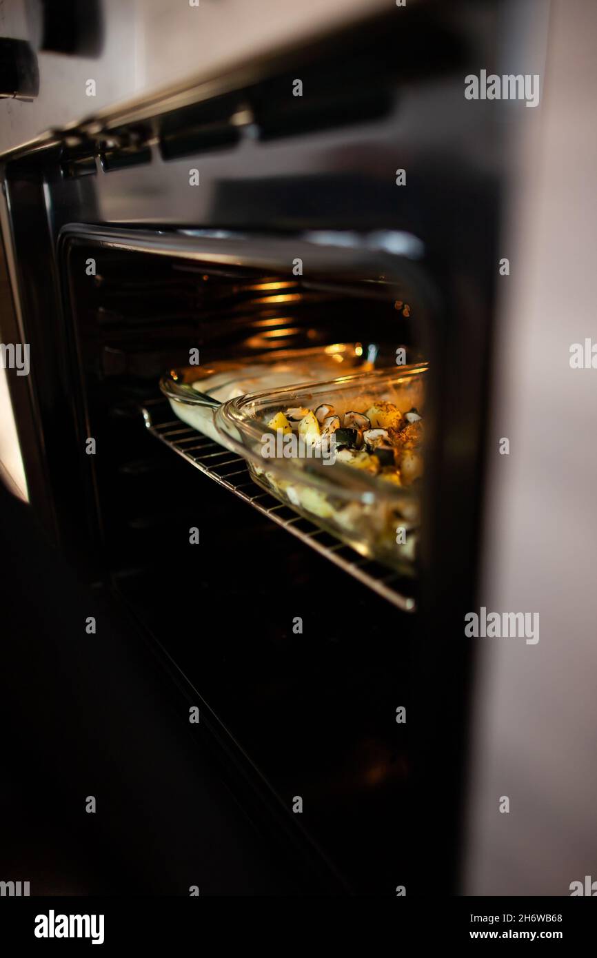 Casserole in glass casserole dish in open oven Close up photo of two casserole dishes in oven with door ajar Delicious meal prep Stock Photo
