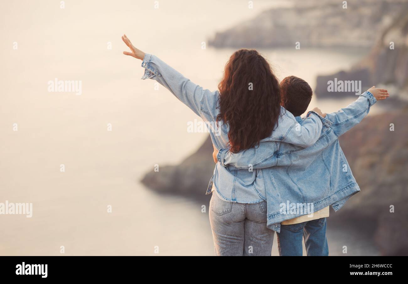 Young mother and her teenage son in denim clothes on the top of mountain, spend time together and hug in spring day Stock Photo