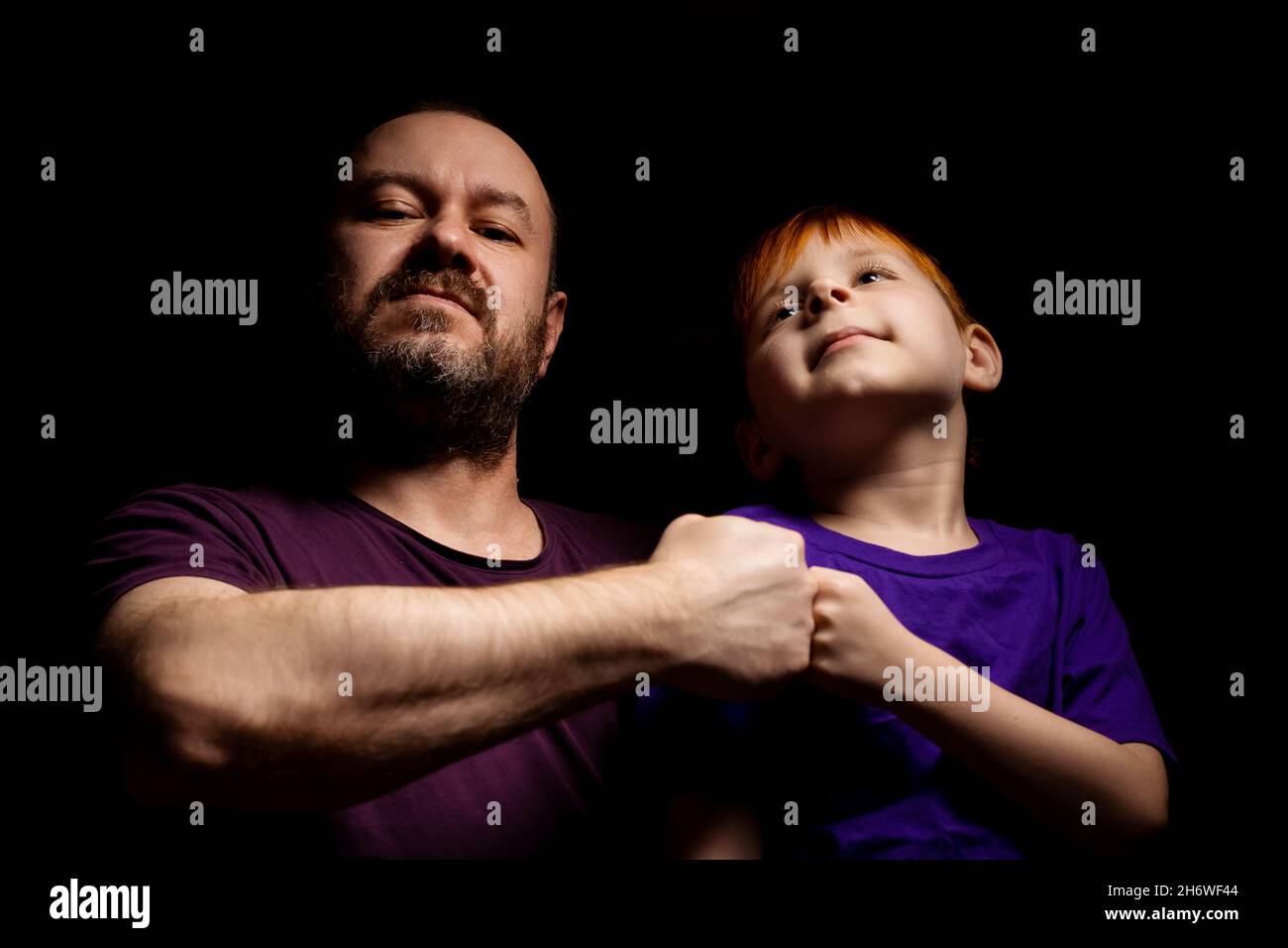 Dad and son are smiling and banging their fists against each other on a black background. Parent