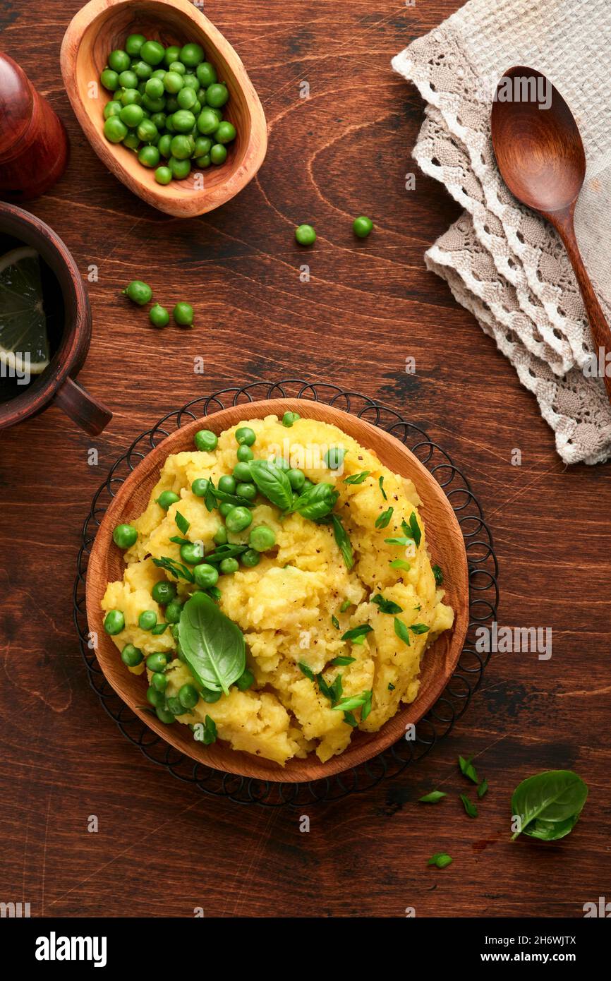 Mashed potato with butter, green peas, onions, basil on a rustic wooden background. Top view with close up. Stock Photo