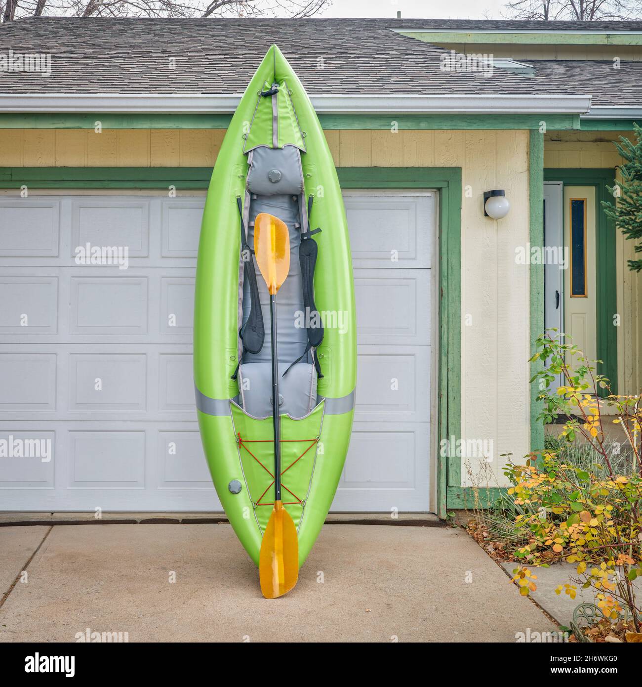 green inflatable whitewater one person kayak with a paddle in a driveway ready for a paddling trip Stock Photo