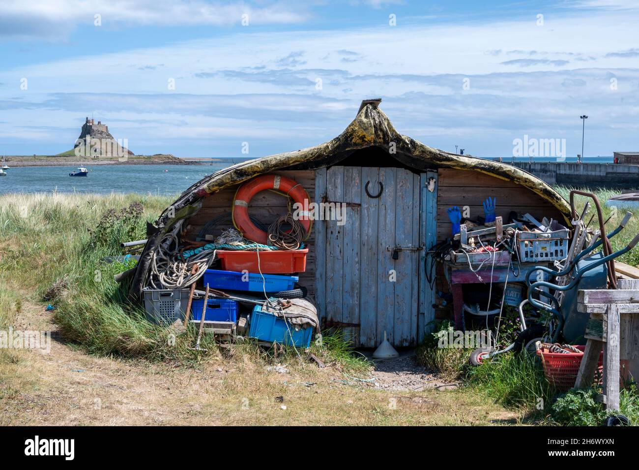 Attractive 'boat sheds' made from repurposed upturned wooden herring boats, Lindisfarne Harbour, Holy Island. Lindisfarne Castle is in the background. Stock Photo
