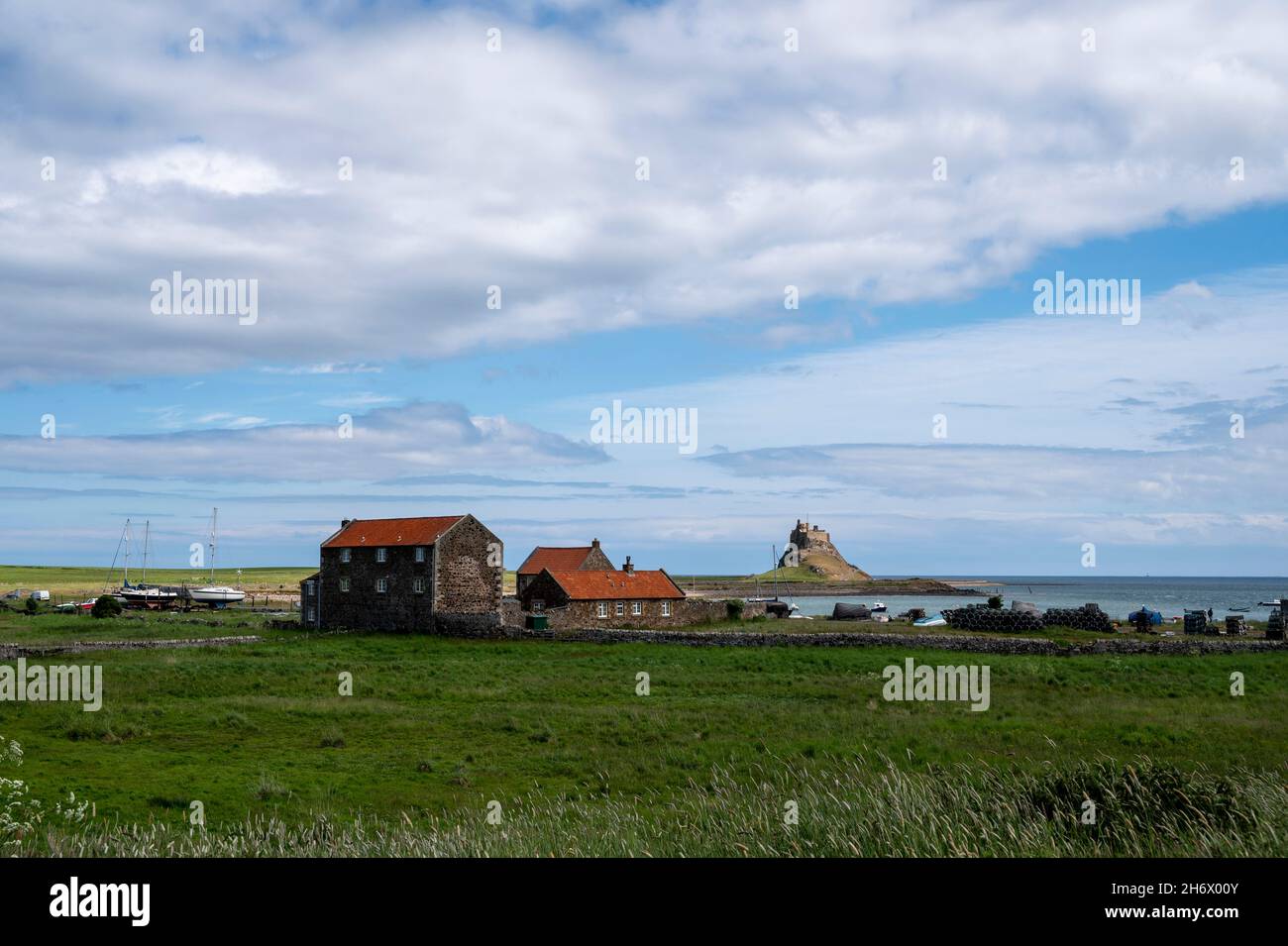 Lindisfarne Harbour, Holy Island, with attractive harbourside buildings, fishing huts and the ancient castle in the background. Stock Photo