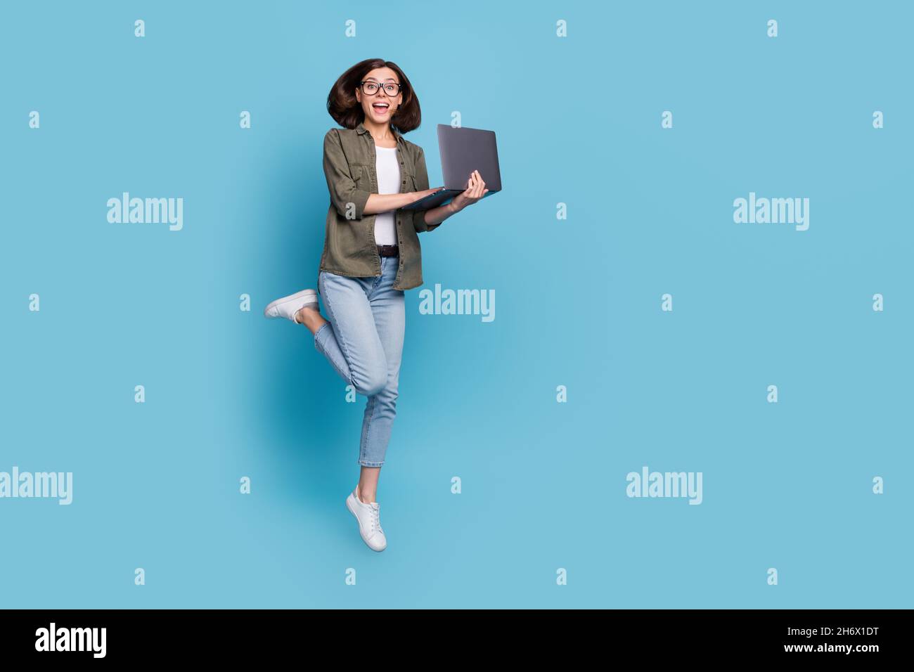 Full length photo of excited lady computer geek it developer jump use gadget wear shirt denim jeans isolated over blue color background Stock Photo