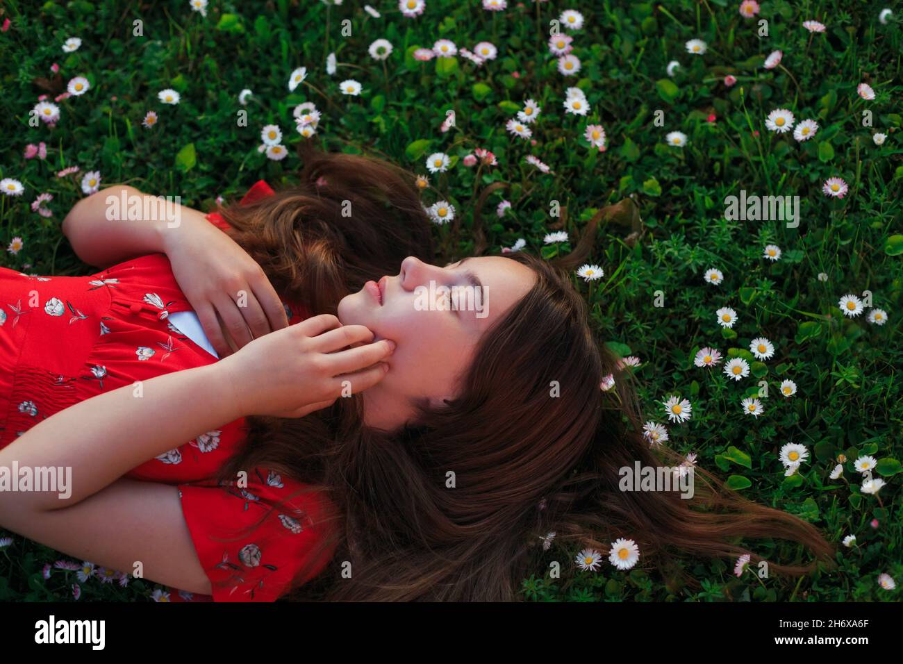 Young beautiful girl in red dress is resting on fresh spring grass Stock Photo