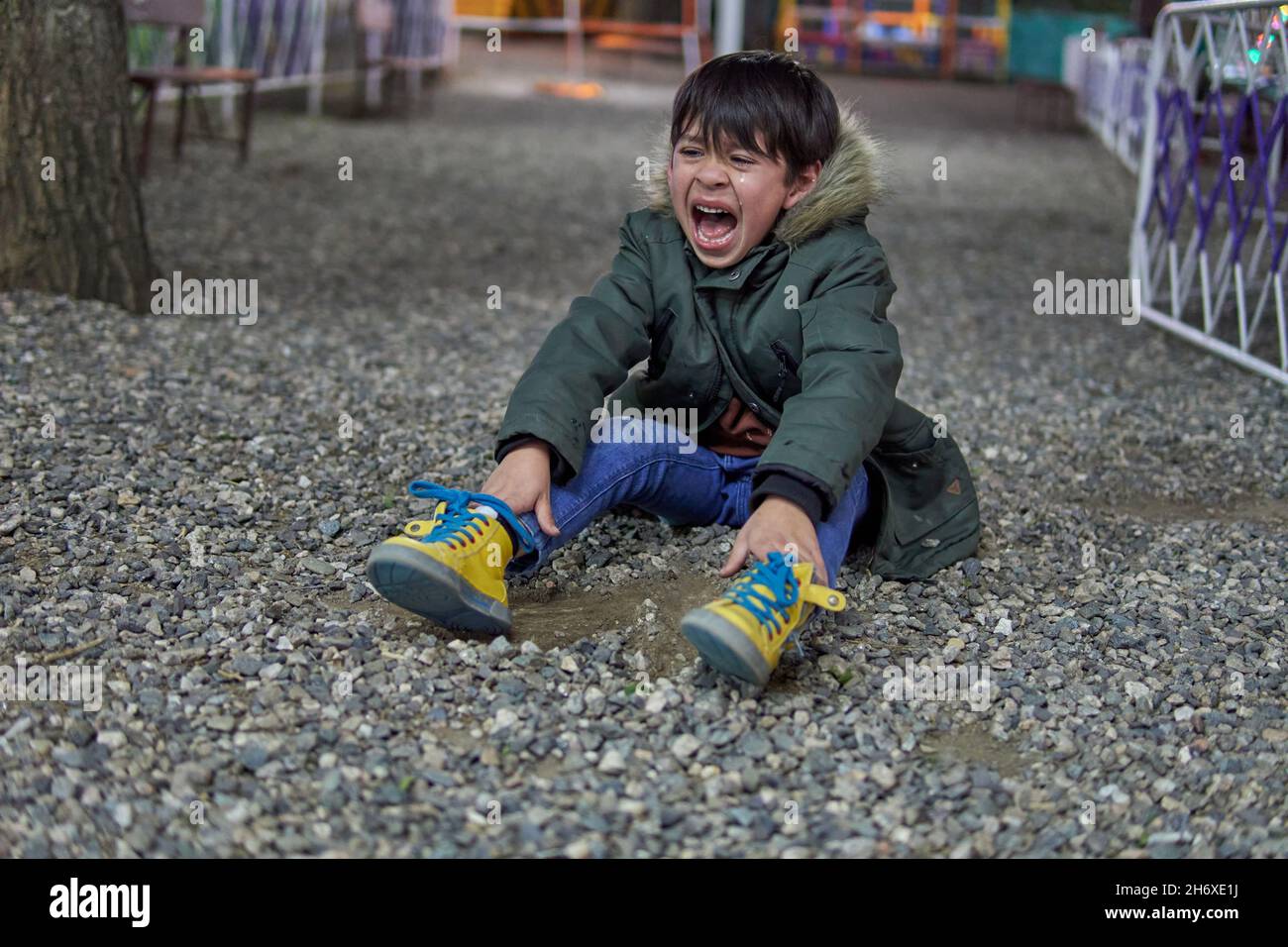 sad and upset child latin boy shouting and crying sitting on the pebble floor in a amusement park. concept for caprice, depression stress or frustrati Stock Photo