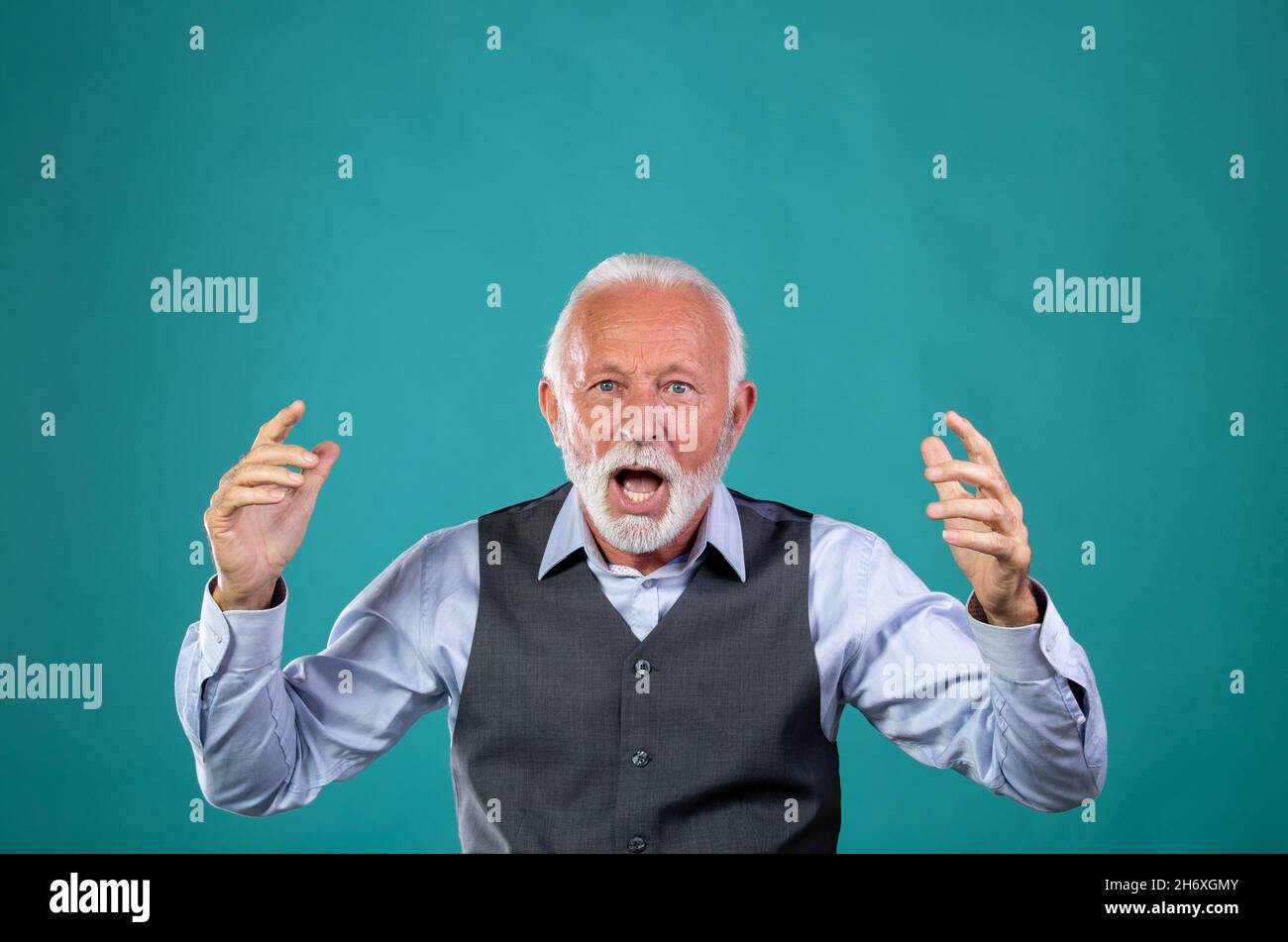 Portrait of old man in business suit yelling, feeling angry, frustrated. Surprised senior citizen with blue eyes and white hair and beard against colo Stock Photo