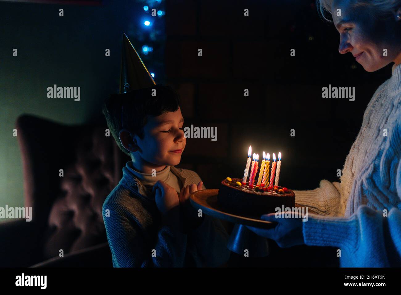 Happy child boy with closed eyes making wish before blowing candles on