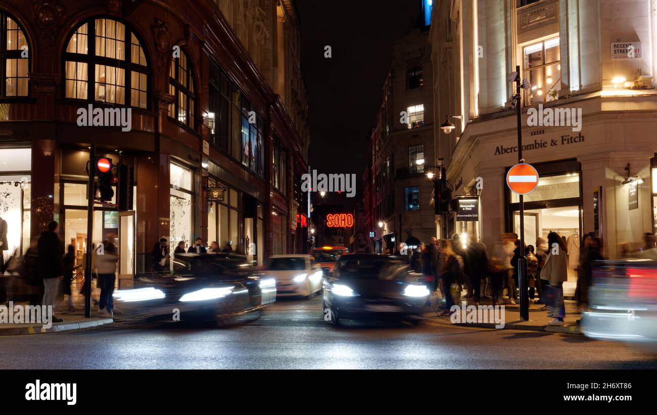 Cars moving away from a junction on Regent Street at night blurred by long exposure, with a Soho sign. London Stock Photo