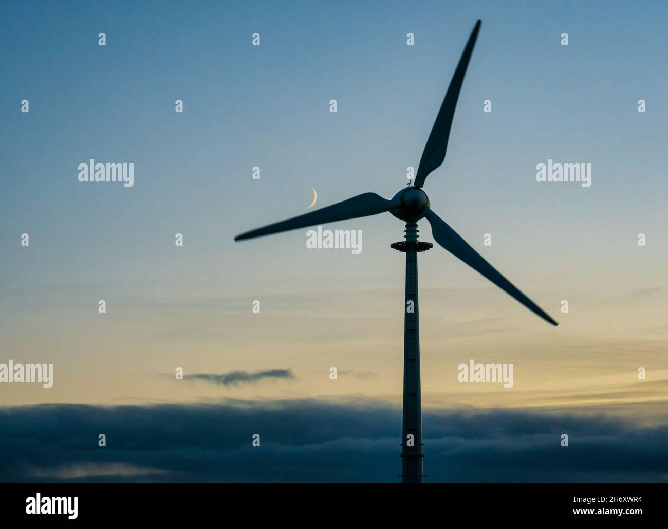 A crescent moon rises the blades of a wind turbine, Scotland, UK Stock Photo