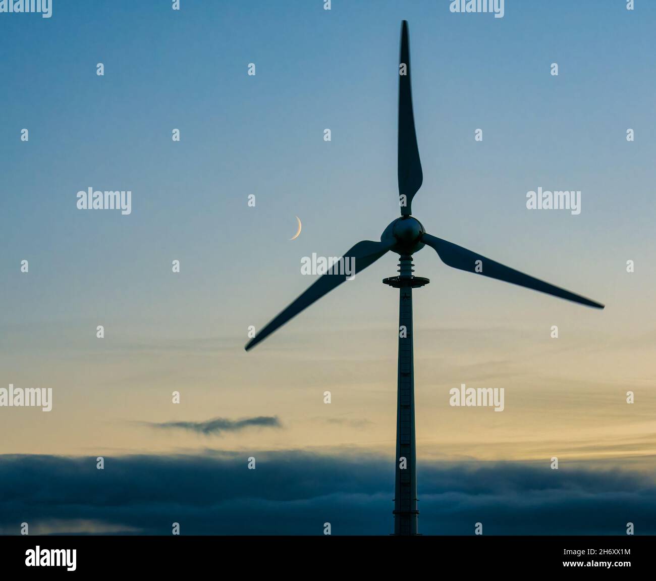 A crescent moon rises above the blades of a wind turbine, Scotland, UK ...