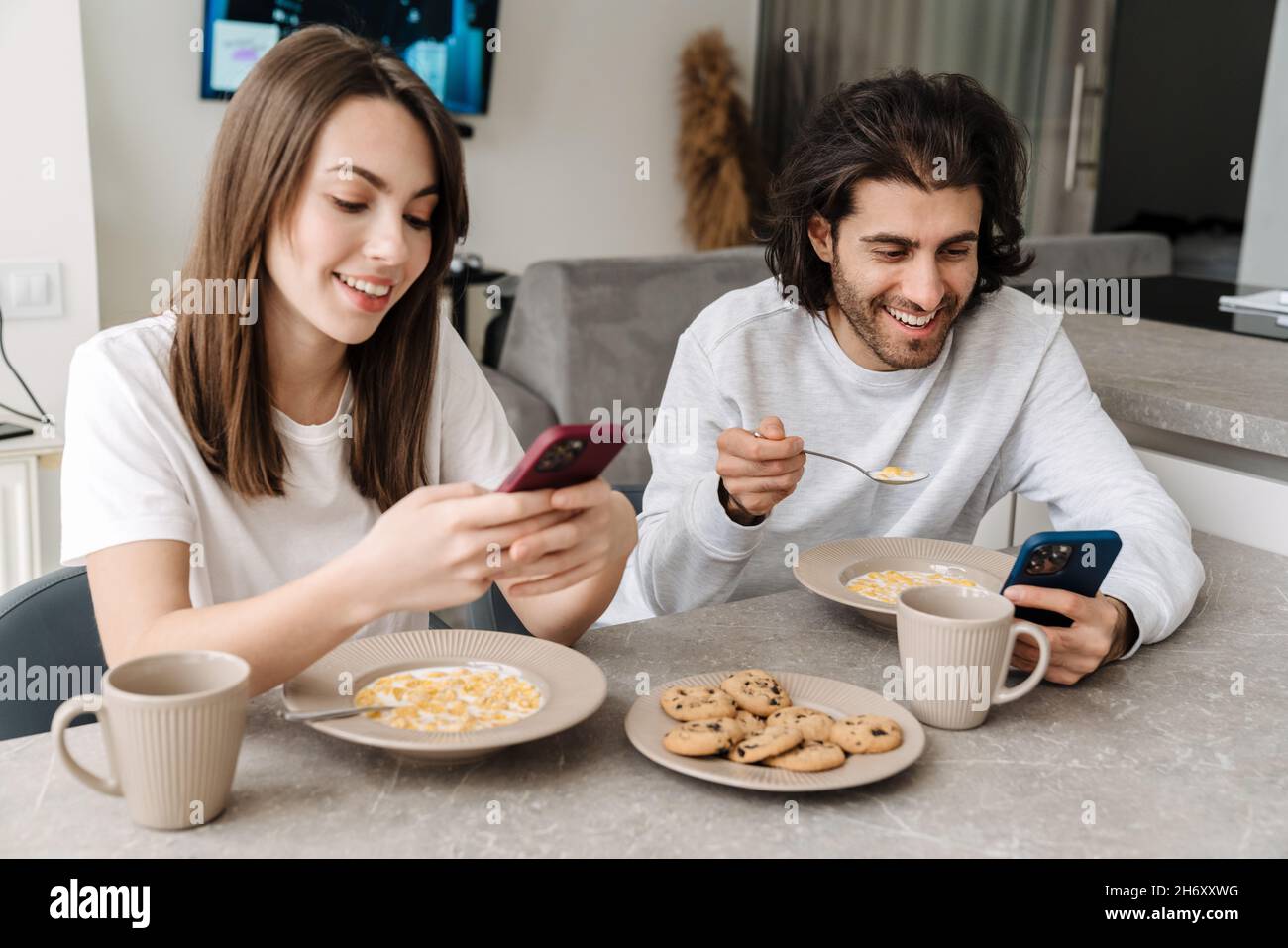 Young multiracial couple using cellphones while having breakfast together at home Stock Photo