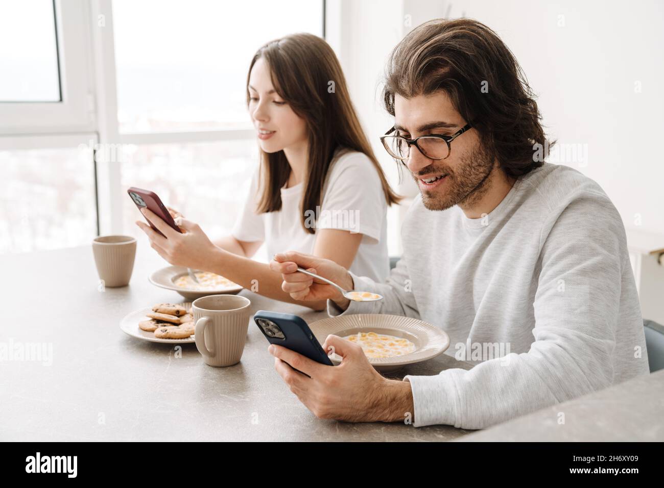 Young multiracial couple using cellphones while having breakfast together at home Stock Photo