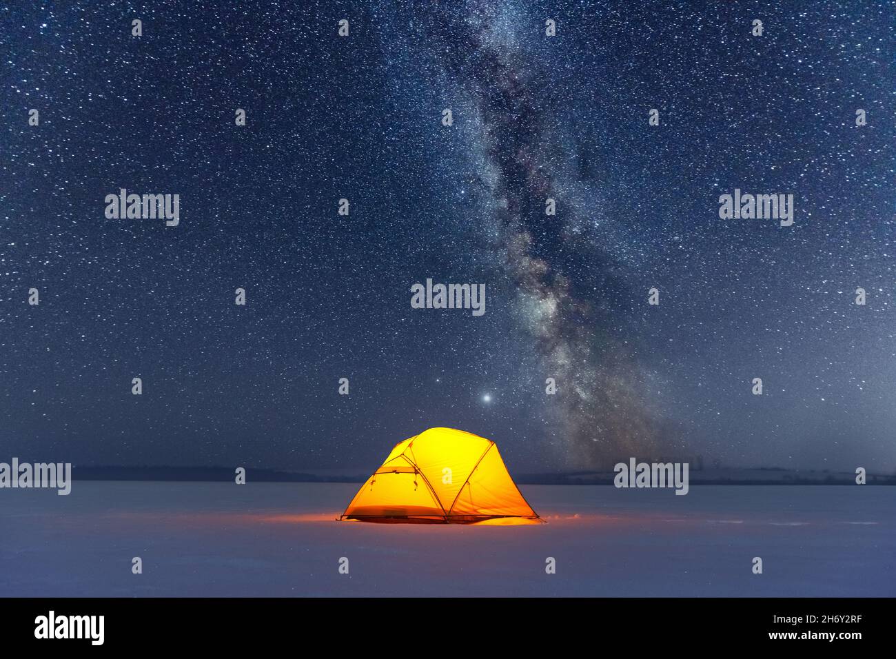 Yellow tent lighted from the inside against the backdrop of incredible starry sky with Milky way. Amazing night landscape. Tourists camp in winter mountains. Travel concept Stock Photo
