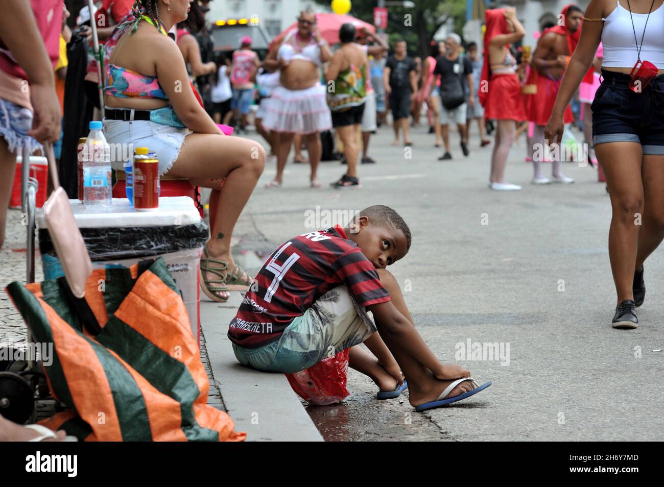 Brazil–February 22, 2020:A boy wearing a Flamengo soccer team jersey observes costumed revelers during a street carnival parade held in Rio de Janeiro Stock Photo