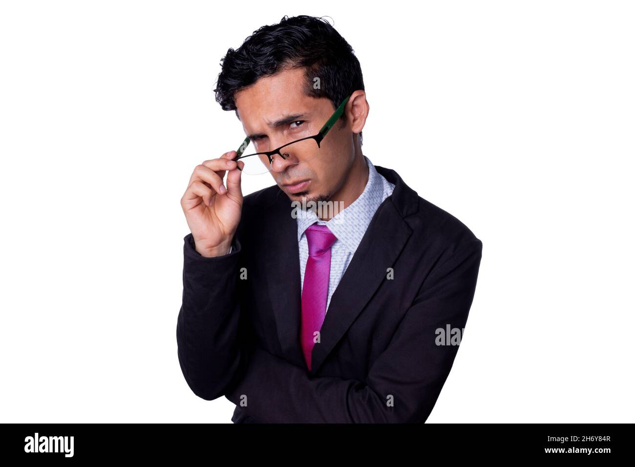 Businessman looking suspiciously at the camera, peering through his glasses with a dubious expression. Young adult latin guy wearing elegant clothes Stock Photo