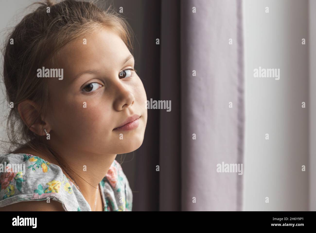 Close up portrait of little Caucasian girl sitting near the window in a ...