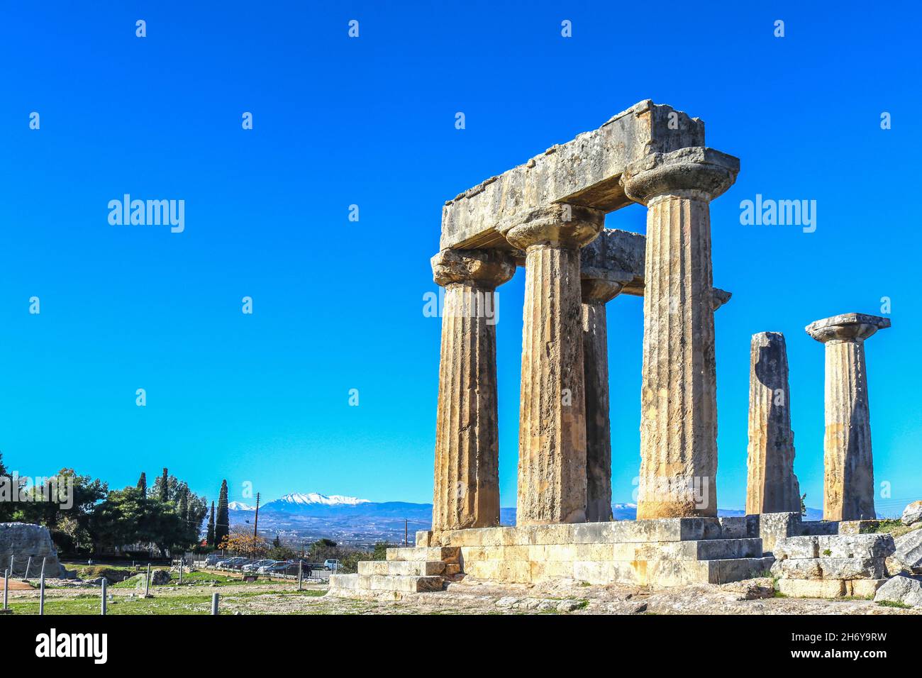 Ruins and columns at Ancient Corinth Greece under extremely blue sky with snow-capped mountains of the mainland across the Corinth Canal in the distan Stock Photo