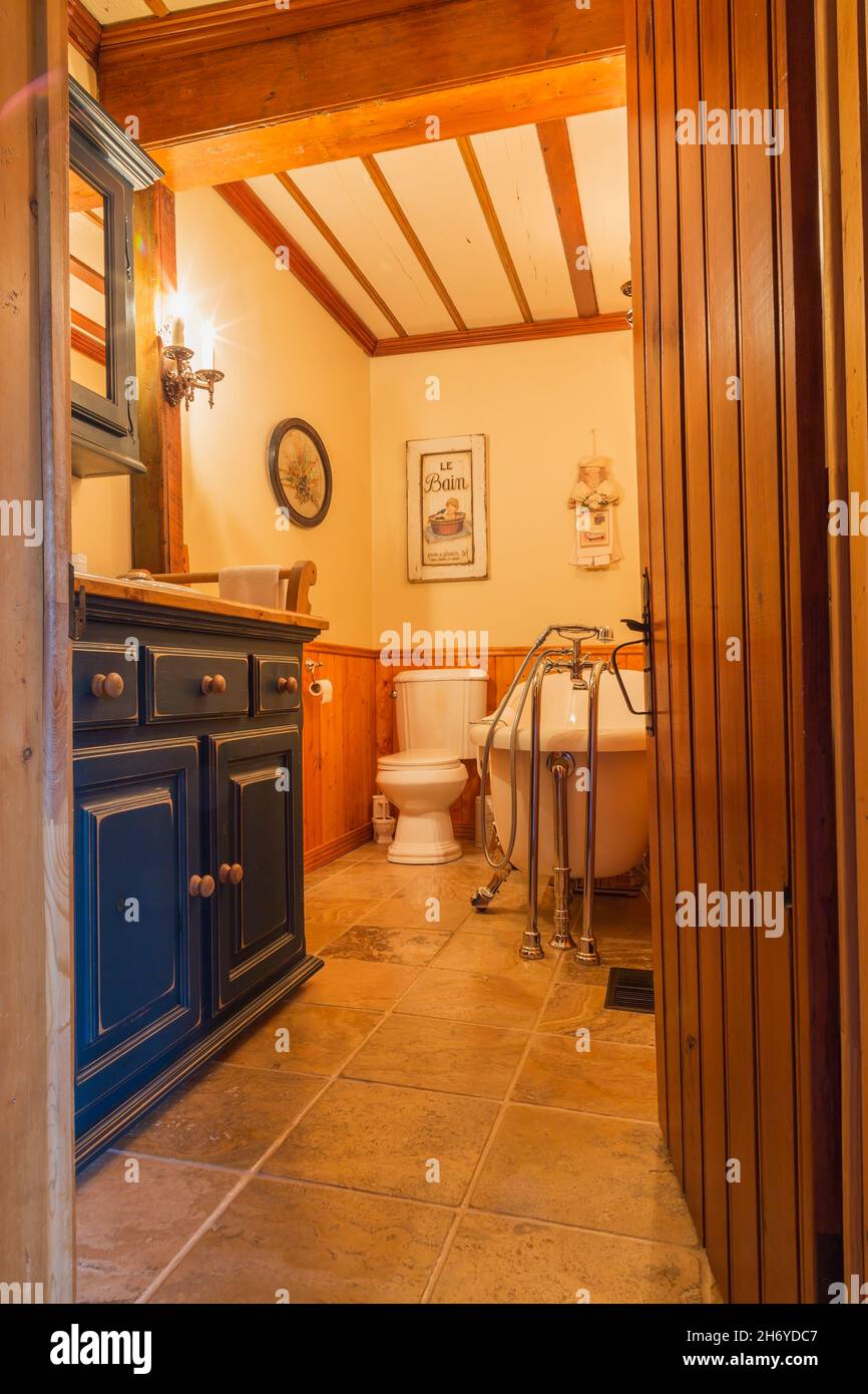 Blue painted wooden vanity and freestanding antique claw foot roll top bathtub in main bathroom inside an old Canadiana circa 1750 home Stock Photo