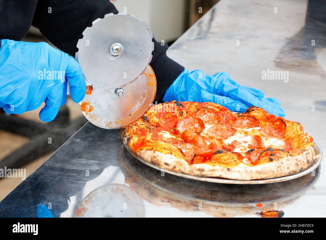 A street chef in blue latex gloves cuts an ovenbaked pizza with a