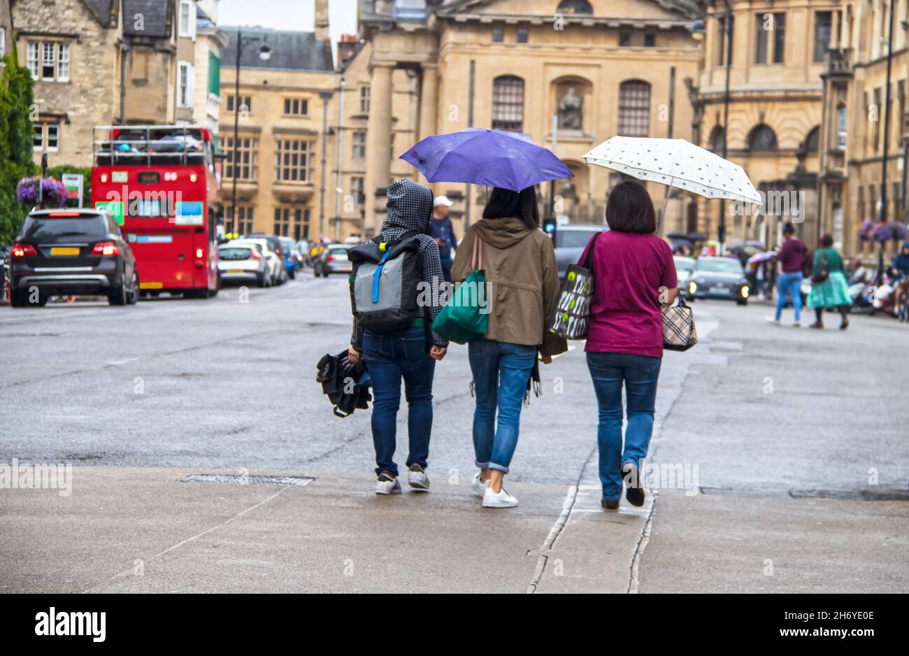 Three women walking away with umbrellas and bags on a rainy day in Oxford England Stock Photo