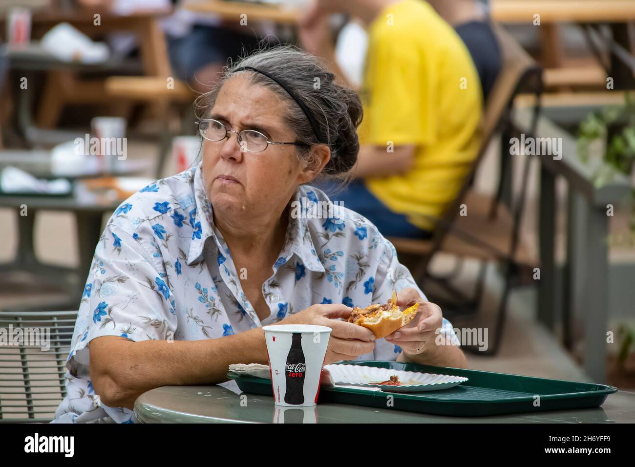 Tulsa USA 9 - 8 2018  Older woman eating a hamburger at an outside table looking up with an unhappy expression on her face Stock Photo