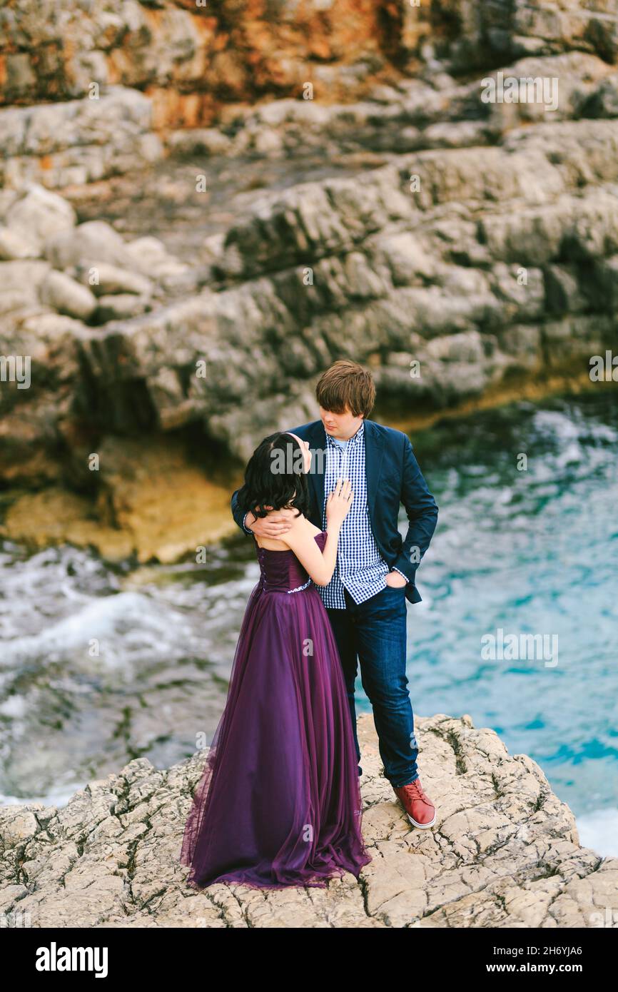 Man hugs woman while standing on a ledge above the sea against a ...